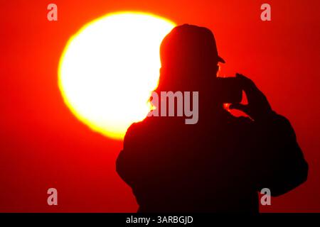 Isle Of Palms, Usa. April 2025. Ein Fotograf mit der Silhouette des Sonnenaufgangs macht Fotos, während die Sonne am Strand des Wild Dunes Resort am 17. April 2025 in Isle of Palms, South Carolina, über den Horizont steigt. Quelle: Richard Ellis/Richard Ellis/Alamy Live News Stockfoto