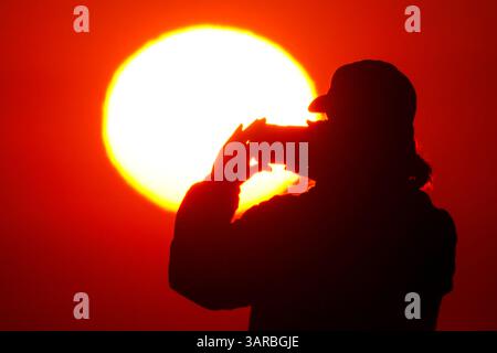 Isle Of Palms, Usa. April 2025. Ein Fotograf mit der Silhouette des Sonnenaufgangs macht Fotos, während die Sonne am Strand des Wild Dunes Resort am 17. April 2025 in Isle of Palms, South Carolina, über den Horizont steigt. Quelle: Richard Ellis/Richard Ellis/Alamy Live News Stockfoto