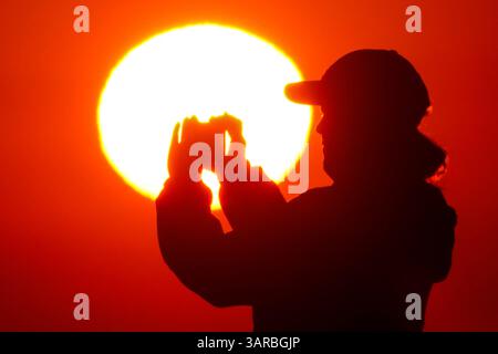 Isle Of Palms, Usa. April 2025. Ein Fotograf mit der Silhouette des Sonnenaufgangs macht Fotos, während die Sonne am Strand des Wild Dunes Resort am 17. April 2025 in Isle of Palms, South Carolina, über den Horizont steigt. Quelle: Richard Ellis/Richard Ellis/Alamy Live News Stockfoto