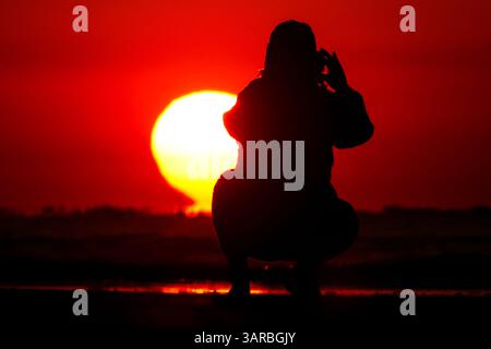 Isle Of Palms, Usa. April 2025. Ein Fotograf mit der Silhouette des Sonnenaufgangs macht Fotos, während die Sonne am Strand des Wild Dunes Resort am 17. April 2025 in Isle of Palms, South Carolina, über den Horizont steigt. Quelle: Richard Ellis/Richard Ellis/Alamy Live News Stockfoto