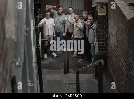 Newcastle, Großbritannien - 12. April 2025 - eine Gruppe fröhlicher männlicher Freunde versammelte sich mit gefühlsmäßig hochgezogenen Daumen und lächelndem Gesicht für ein Porträt auf der Treppe Stockfoto