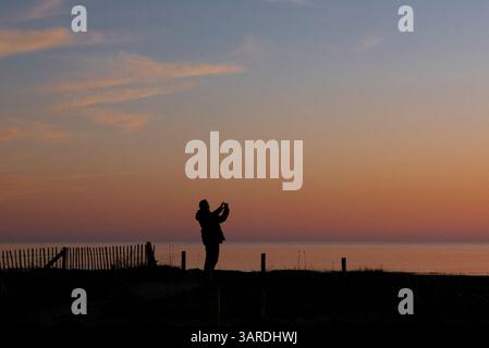 Silhouette eines Mannes, der ein Foto von einem farbigen Sonnenuntergang aus dem Morbihan Golf in der Bretagne (Morbihan), Frankreich, macht. Stockfoto