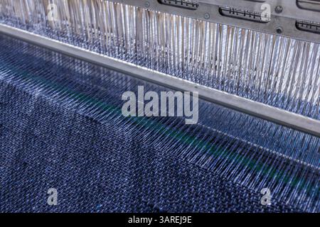Detaillierte Ansicht eines automatisierten Webstuhls, der dunkelblaues Textilgewebe mit präziser Fadenausrichtung herstellt. Stockfoto