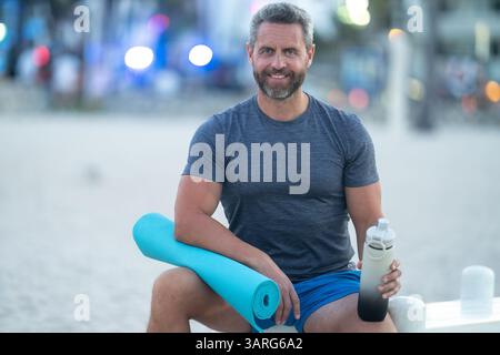 Sport-Fitness-Mann, der draußen auf einer Bank ruht. Reifes Fitnesssportmodell, das nach dem Training auf einer Bank sitzt. Senior Sports man macht danach eine Pause Stockfoto