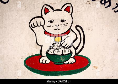 Maneki-neko-Katze mit einer Schüssel Momos von einem japanisch inspirierten Café-Schild, das ostasiatische Ikonographie mit Himalaya-Motiven verbindet. Stockfoto