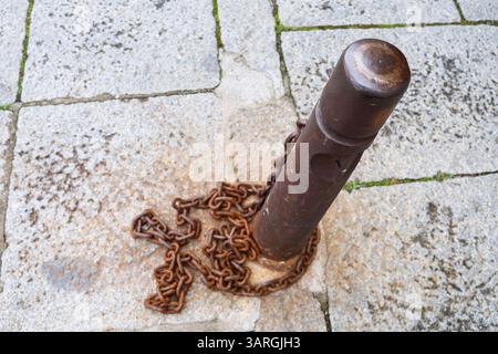 Sicherheitsdrehpunkt mit Rusty Ketten auf Steinboden auf der Straße in Spanien Stockfoto