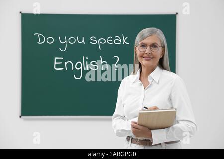 Lehrer bei grüner Tafel mit Phrase sprichst du Englisch? Im Klassenzimmer Stockfoto