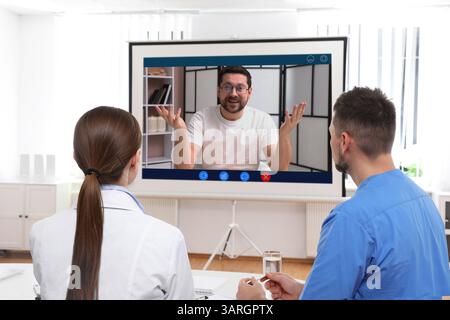 Redner, der über Online-Videochat an der Vorlesung teilnimmt. Medizinisches Personal im Konferenzraum mit Projektionsleinwand Stockfoto
