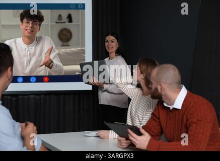 Redner, der über Online-Videochat an der Vorlesung teilnimmt. Publikum und Trainer im Konferenzraum mit Projektionsleinwand Stockfoto