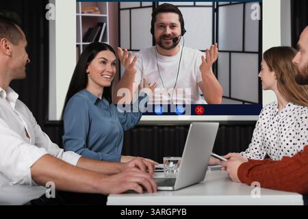 Redner, der über Online-Videochat an der Vorlesung teilnimmt. Publikum im Konferenzraum mit Projektionsleinwand Stockfoto