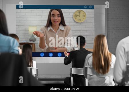 Redner, der über Online-Videochat an der Vorlesung teilnimmt. Publikum im Konferenzraum mit Projektionsleinwand Stockfoto