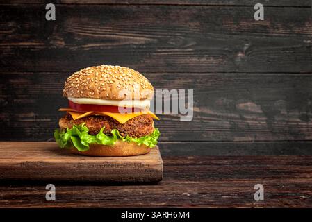 Hausgemachter Hähnchenburger mit Salat, Käse, Sauce und Tomate auf rustikalem dunklem Holzhintergrund, Kopierraum. Stockfoto