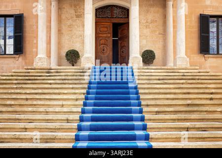 Majestätische Treppe mit blauem Teppich führt zum Eingang eines alten Gebäudes mit geschnitzter Holztür, Steinsäulen und Fensterläden. Stockfoto