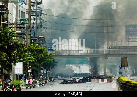 16. Mai 2010 - Bangkok, Thailand - Rauch steigt über der Skyline von Bangkok an brennenden Reifenbarrikaden entlang der Rama IV Road in der Nähe des Lumpini Boxstadions Sonntag. Thailändische Truppen und regierungsfeindliche Demonstranten stießen am Sonntagnachmittag erneut in einer Reihe von Schlachten auf der Rama IV Road zusammen. Truppen feuerten in die Luft und nicht identifizierte Scharfschützen schossen auf Fußgänger auf den Gehwegen. Irgendwann sagte die Regierung, sie werde eine Ausgangssperre verhängen, nur um die Ankündigung Stunden später aufzuheben. Die Lage in Bangkok verschlechtert sich weiter, da sich die Proteste über den Bereich der Red-Shirts-Bühne bei Ratte ausbreiteten Stockfoto