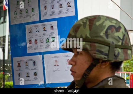 16. Mai 2010 - Bangkok, Thailand - Ein thailändischer Soldat steht vor einem Poster von Anführern der gesuchten Roten Hemden an einem Armeebesuchpunkt auf der Sukhumvit Road in Soi 2 Sonntag. Thailändische Truppen und regierungsfeindliche Demonstranten stießen am Sonntagnachmittag erneut in einer Reihe von Schlachten auf der Rama IV Road zusammen. Truppen feuerten in die Luft und nicht identifizierte Scharfschützen schossen auf Fußgänger auf den Gehwegen. Irgendwann sagte die Regierung, sie werde eine Ausgangssperre verhängen, nur um die Ankündigung Stunden später aufzuheben. Die Lage in Bangkok verschlechtert sich weiter, da sich die Proteste über den Bereich der Red-Shirts-Bühne hinaus ausbreiteten Stockfoto