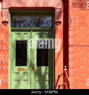 Mintgrüne Doppeltür mit erhöhten Paneelen und Heckfenster vor einer detailreichen roten Backsteinfassade in Chicago Stockfoto