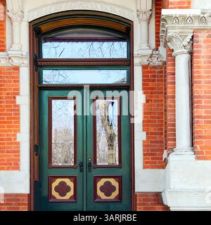 Dekorative grüne Doppeltür mit Glaspaneelen und kunstvollen Wappenakzenten, eingerahmt von Bogensteinwerk und roten Backsteinen in einem historischen Chicago-Gebäude Stockfoto
