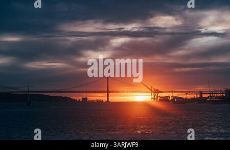 Malerisches Bild des Sonnenuntergangs von der '25 de Abril Bridge' und den Kränen des Stadthafens in Lissabon Ende März. Stockfoto