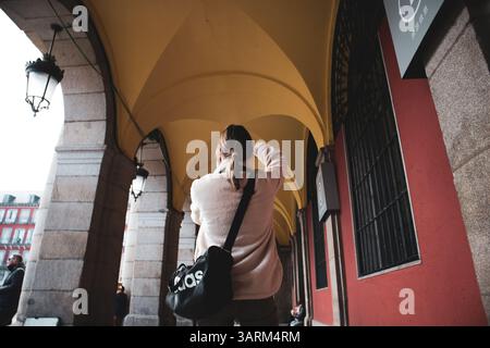 Eine Person mit einer Tasche geht durch einen Bogengang mit Steinsäulen und einer roten Wand, aufgenommen aus einer niedrigen Perspektive. Weibliche Touristin in Europa. Stockfoto
