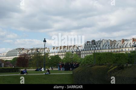 Die Menschen entspannen sich auf den grünen Rasenflächen des Tuilerien-Gartens in Paris, mit klassischer Pariser Architektur, die eine malerische Kulisse unter einem bewölkten Himmel bildet. Stockfoto