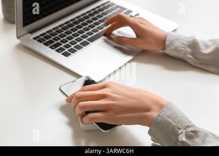 Frau, die das Mobiltelefon auf ein kabelloses Ladegerät stellt, während sie mit dem Laptop auf dem Lichttisch arbeitet, Nahaufnahme Stockfoto