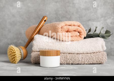 Stapel von sauberen Handtüchern, Massagebürste und Kosmetikprodukten auf Grunge-Hintergrund Stockfoto