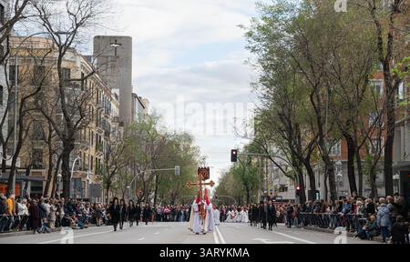 Madrid, Spanien. April 2025. Panoramablick auf eine Karwochenprozession mit Nazarenern, die ein großes, reich verziertes Kreuz durch eine breite Straße der Stadt tragen. Die Karwochenprozession in Madrid ist eine tief verwurzelte katholische Tradition, die in der Woche vor Ostern stattfindet. Mit feierlichen Paraden mit religiösen Wagen, traditioneller Musik und Teilnehmern in Bußgewändern spiegelt die Veranstaltung das reiche spirituelle Erbe Spaniens wider und zieht jedes Jahr Tausende von Zuschauern an. Quelle: SOPA Images Limited/Alamy Live News Stockfoto