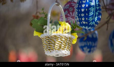 Eine bezaubernde Osterszene mit einem kleinen Blumenkorb voller Blüten. Dekorative, gemusterte Eier hängen im Hintergrund und verleihen festliche Akzente Stockfoto