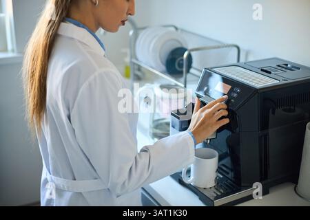 Barista bereitet Kaffee in einer modernen automatischen Kaffeemaschine in einer Küche zu. Person mit weißem Laborkittel und neben der Kaffeemaschine Stockfoto