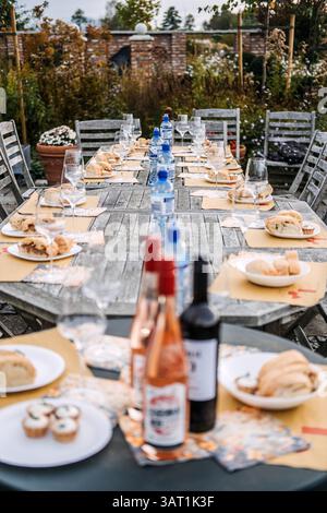 Langer rustikaler Holztisch für eine Gartenmahlzeit mit Brot, Wein und Sprudelwasser unter Herbsthimmel. Rustikales Essen, saisonale Feierlichkeiten Stockfoto
