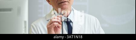 Porträt eines erfahrenen älteren männlichen Arztes mit Mikrofon im Labormantel. Scheinbare medizinische Umgebung mit Technik Stockfoto