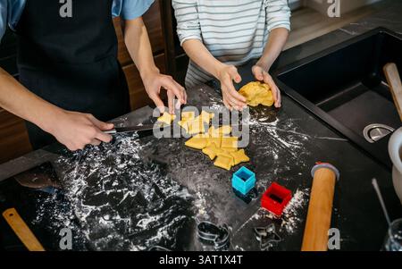 Nicht erkennbare Kinder, die Kekse mit verschiedenen Formen auf einer unordentlichen Küchentheke machen Stockfoto
