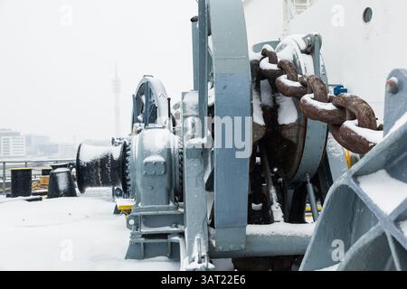 Das Anlegedeck eines Frachtschiffes mit Ankerwinden, einer Ankerkette an Winden, Pollern und Haws mit Anlegeseilen, gefroren und mit Schnee bedeckt. Sn Stockfoto