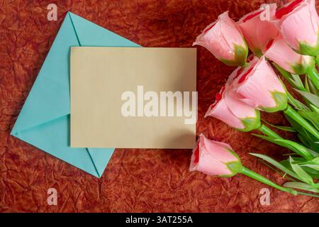 Rosafarbene Rosen werden auf einer reichen Oberfläche neben einer leeren Karte und einem Umschlag platziert und erinnern an Themen wie Liebe, Romantik und innige Verbindung. Stockfoto