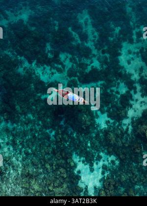 Holzboot schwimmt über einem flachen Korallenriff in der Nähe felsiger Formationen im kristallklaren blauen Wasser in Thailand. Stockfoto