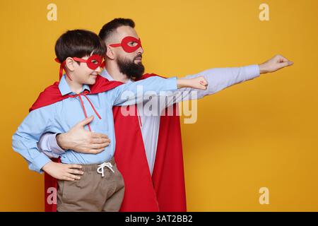Vater und Sohn tragen Superheldenkostüme auf orangem Hintergrund Stockfoto
