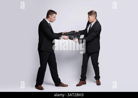 Wettbewerbskonzept. Geschäftsleute ziehen Lederaktentasche auf grauem Hintergrund Stockfoto