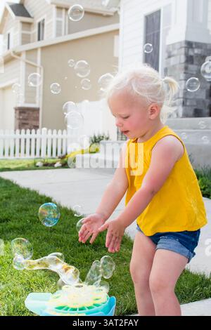 Kleinkind in gelbem Oberteil und Shorts spielt an sonnigen Tagen mit Luftblasen Stockfoto