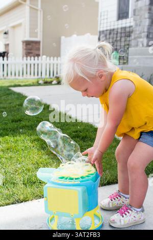 Kleinkind in gelbem Oberteil und Shorts spielt an sonnigen Tagen mit Luftblasen Stockfoto