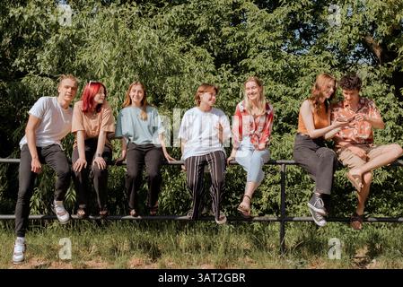 Teenager sitzen und unterhalten sich am Zaun im sonnigen Park Stockfoto