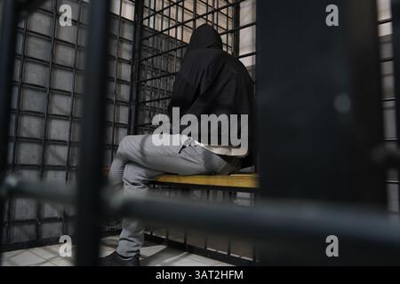 Ein Häftling mit Kapuze sitzt in einer geschlossenen, vorübergehenden Zelle. Stockfoto