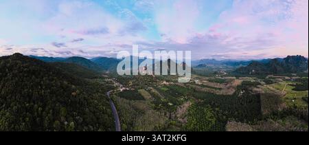 Panoramablick auf den Khao Sok Nationalpark in Thailand, mit Kalksteinbergen, dichtem Regenwald und Ackerland unter einem farbenfrohen Sonnenaufgangshimmel. Stockfoto