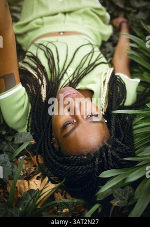 Eine schwarze Frau mit Afro-Zöpfen liegt in einem grünen Dickicht Stockfoto