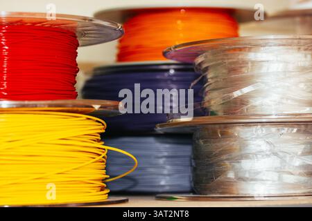Bunte Filamentspulen für den 3D-Druck sind gestapelt und zeigen leuchtende Rot-, Orangen-, Gelb- und Blautöne. Jeder Schieber ist ordentlich auf einer transparenten Rolle aufgewickelt. Stockfoto