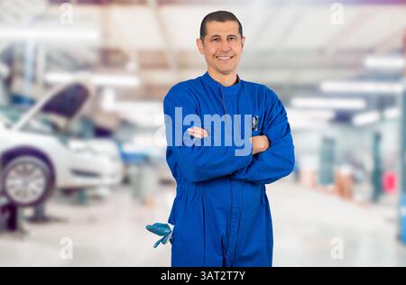 Porträt eines selbstbewussten, ausgereiften Mechanikers in Overalls mit überkreuztem Arm und Blick auf die Kamera in der Werkstatt. Stockfoto