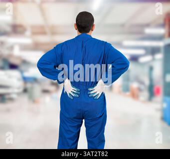 Rückansicht eines Mechanikers, der seinen unteren Rücken wegen Schmerzen im Werk hält Stockfoto