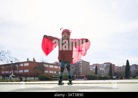 Mädchen trägt Marienkäfer-Kostüm mit Helm und Schutz Rollschuhlaufen in einem Park, hat Spaß und spielt wie ein Superheld Stockfoto