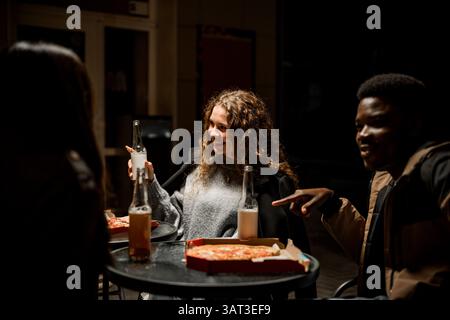 Freunde genießen abends Pizza und Getränke in einem gemütlichen Treffpunkt vor Ort Stockfoto