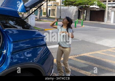 Ein Teenager steht neben einem blauen Auto mit geöffnetem Kofferraum. Sie sieht sich etwas im Auto an Stockfoto