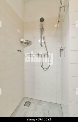 Eine moderne Duschkabine mit sauberen, weiß gefliesten Wänden und einem eleganten Duschkopf. Das Design betont Einfachheit und Funktionalität. Stockfoto